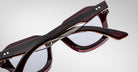 Detailed back view of a pair of Jacques Marie Mage Eichler cherry color, thick-framed sunglasses with lilac lenses on a plain background