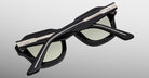 The Jacques Marie Mage Eichler sunglasses are shown upside down against a gray background, showcasing their black frames, light-tinted lenses, and distinctive metallic detailing on the arms and top of the frame.