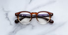 Jacques Marie Mage Eiko round eyeglasses, brown and clear frame, black arms. Front angle view.