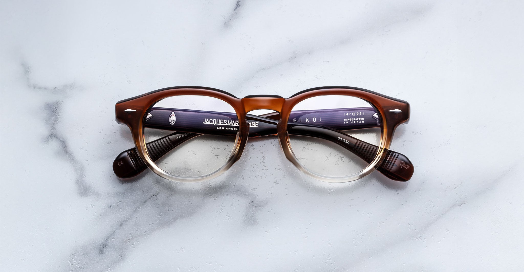 Jacques Marie Mage Eiko round eyeglasses, brown and clear frame, black arms. Front angle view.