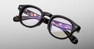 Jacques Marie Mage Eiko eyeglasses, black round frames with clear lenses and inner arm metal accents, front view.