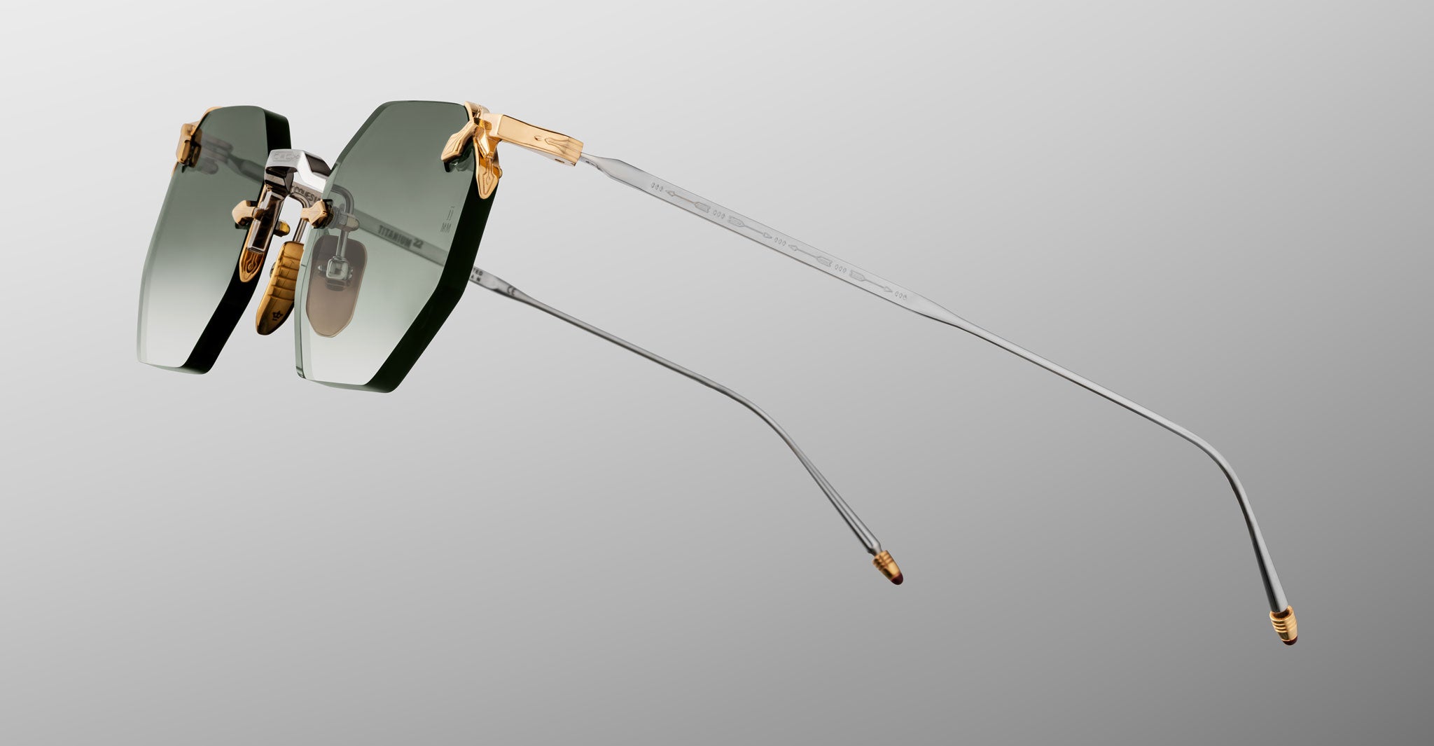 The Jacques Marie Mage El Dorado features rimless sunglasses with rectangular green-tinted lenses, gold accents at the hinges and nose bridge, and thin silver metal arms, shown against a gray gradient background.