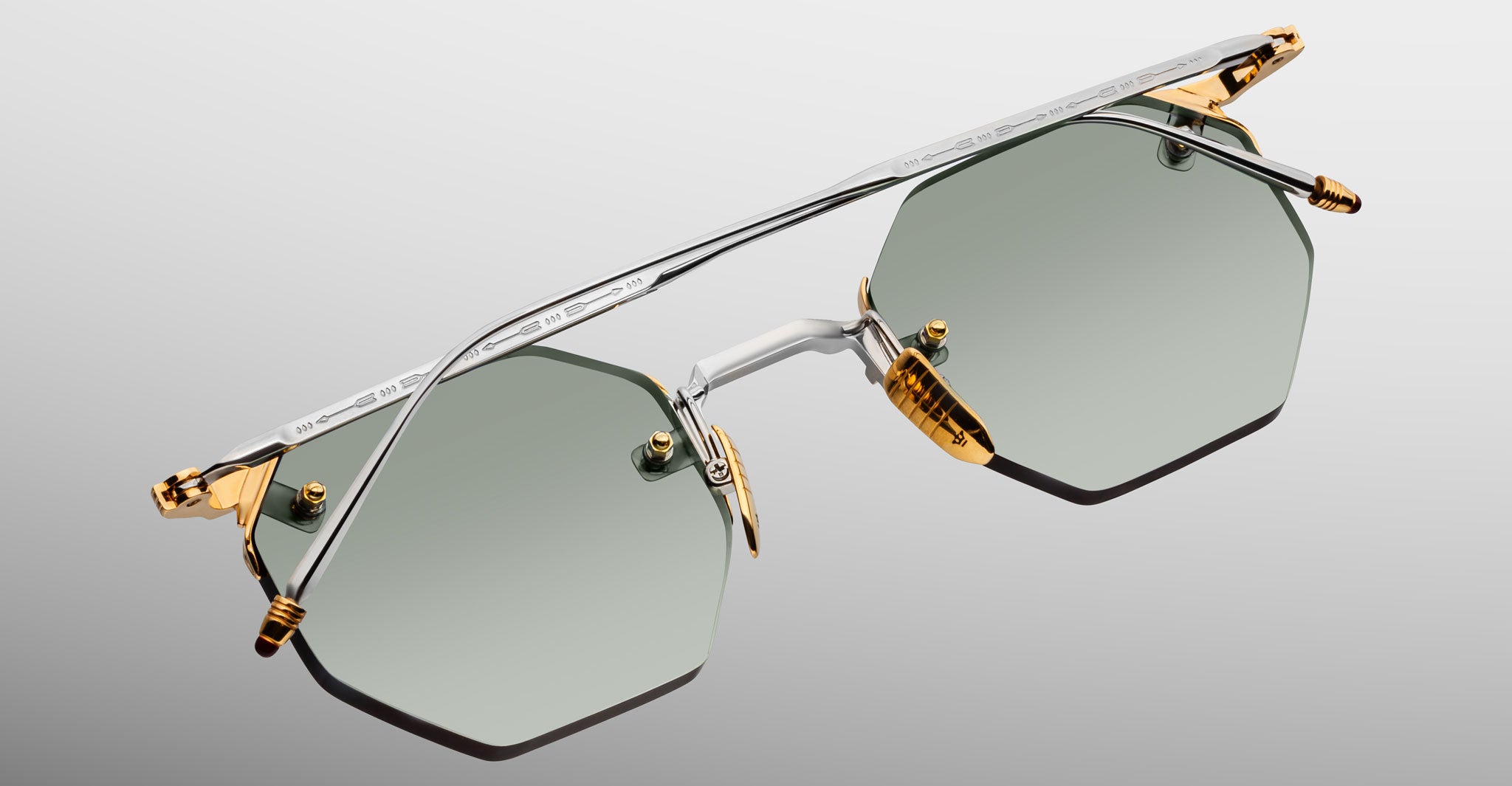 The Jacques Marie Mage El Dorado sunglasses feature geometric hexagonal frames in silver and gold metal, green-tinted lenses, and gold accents on the nose bridge and hinges, shown against a light gray background.