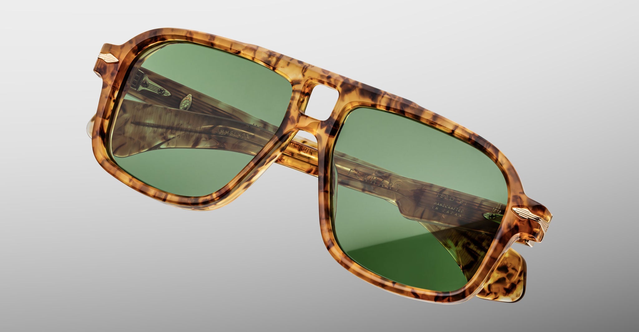 The Jacques Marie Mage Elkhart is a limited-edition oversized navigator sunglass with a brown tortoiseshell frame, sculpted brow ridge, and green lenses, shown against a plain light gray background.