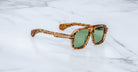 Jacques Marie Mage Elkhart limited-edition navigator sunglasses with a sculptural brow ridge and green tinted lenses, displayed on a white marble surface.
