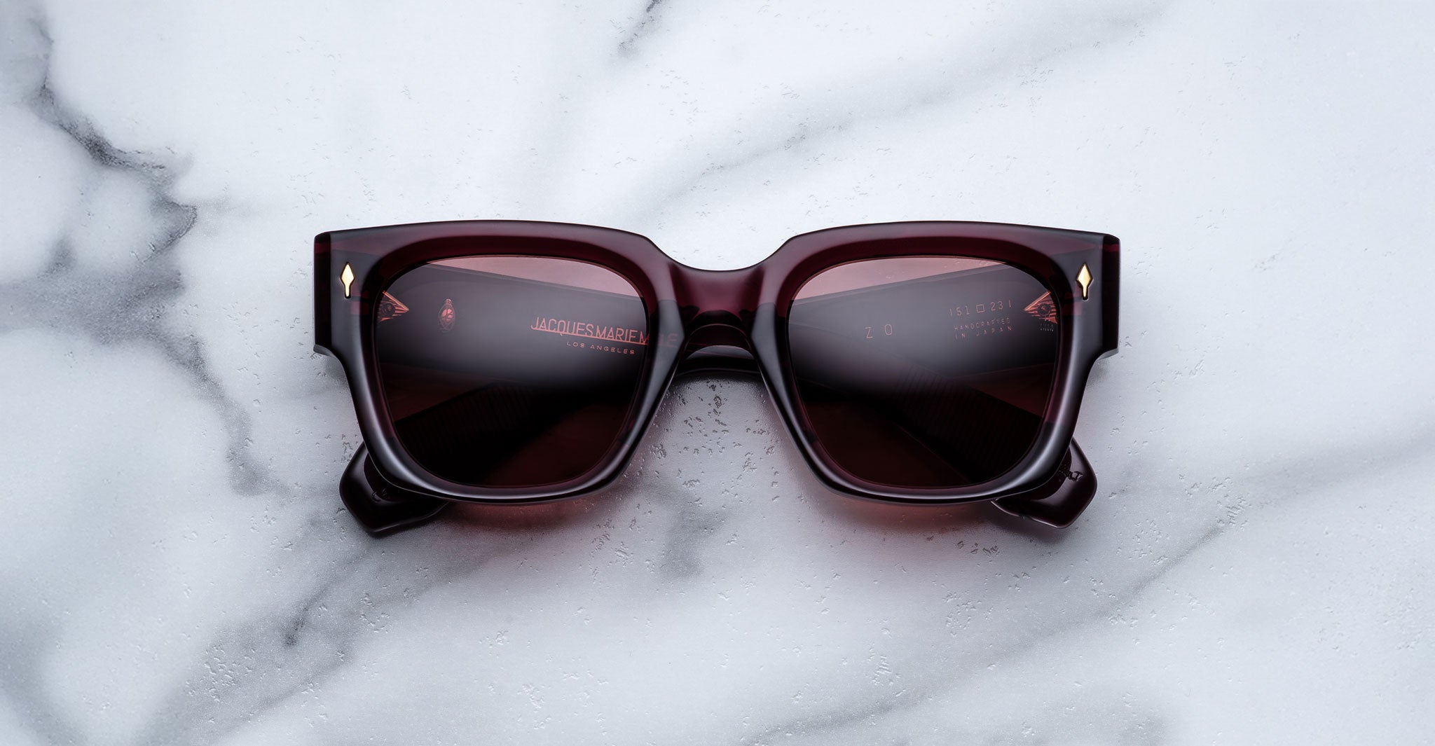 Jacques Marie Mage Enzo dark red square sunglasses with tinted lenses, shown from above.