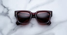 Jacques Marie Mage Enzo dark red square sunglasses with tinted lenses, shown from above.