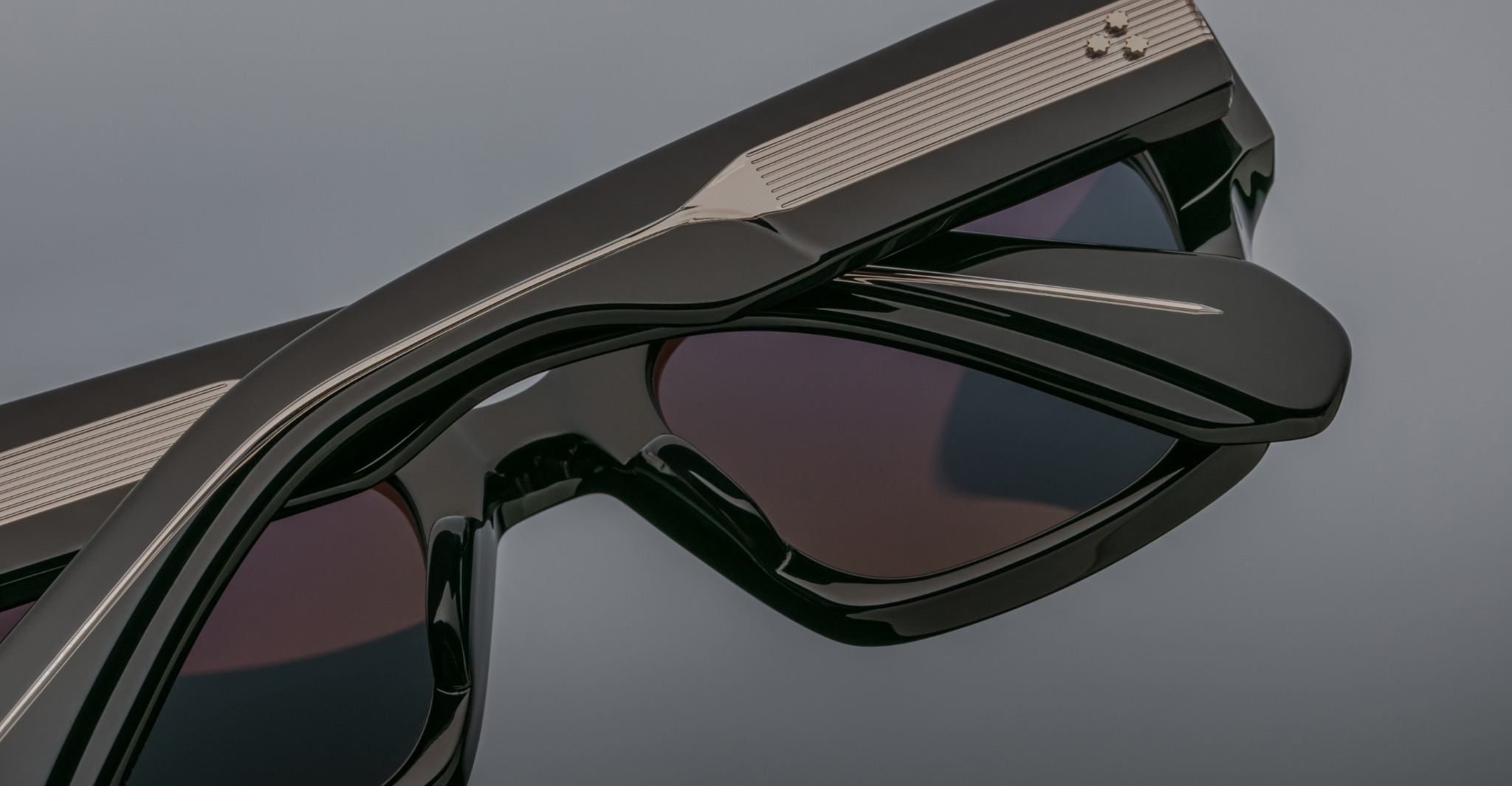 Close-up of stacked Jacques Marie Mage Enzo black polarized sunglasses with dark lenses, viewed from above.