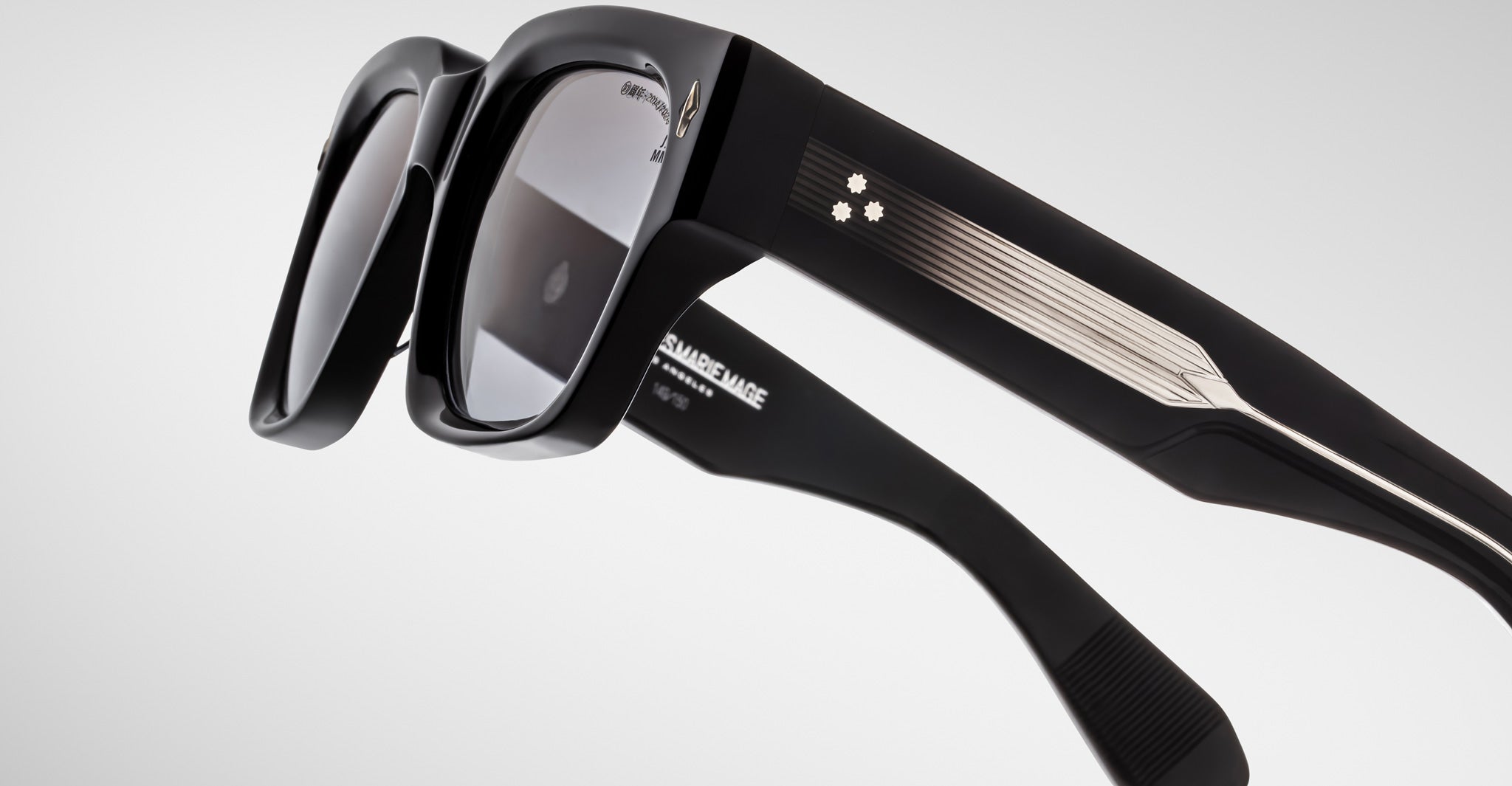 Close-up of Jacques Marie Mage Enzo black sunglasses showing metallic accents, polarized lenses, and star motif on the temple.
