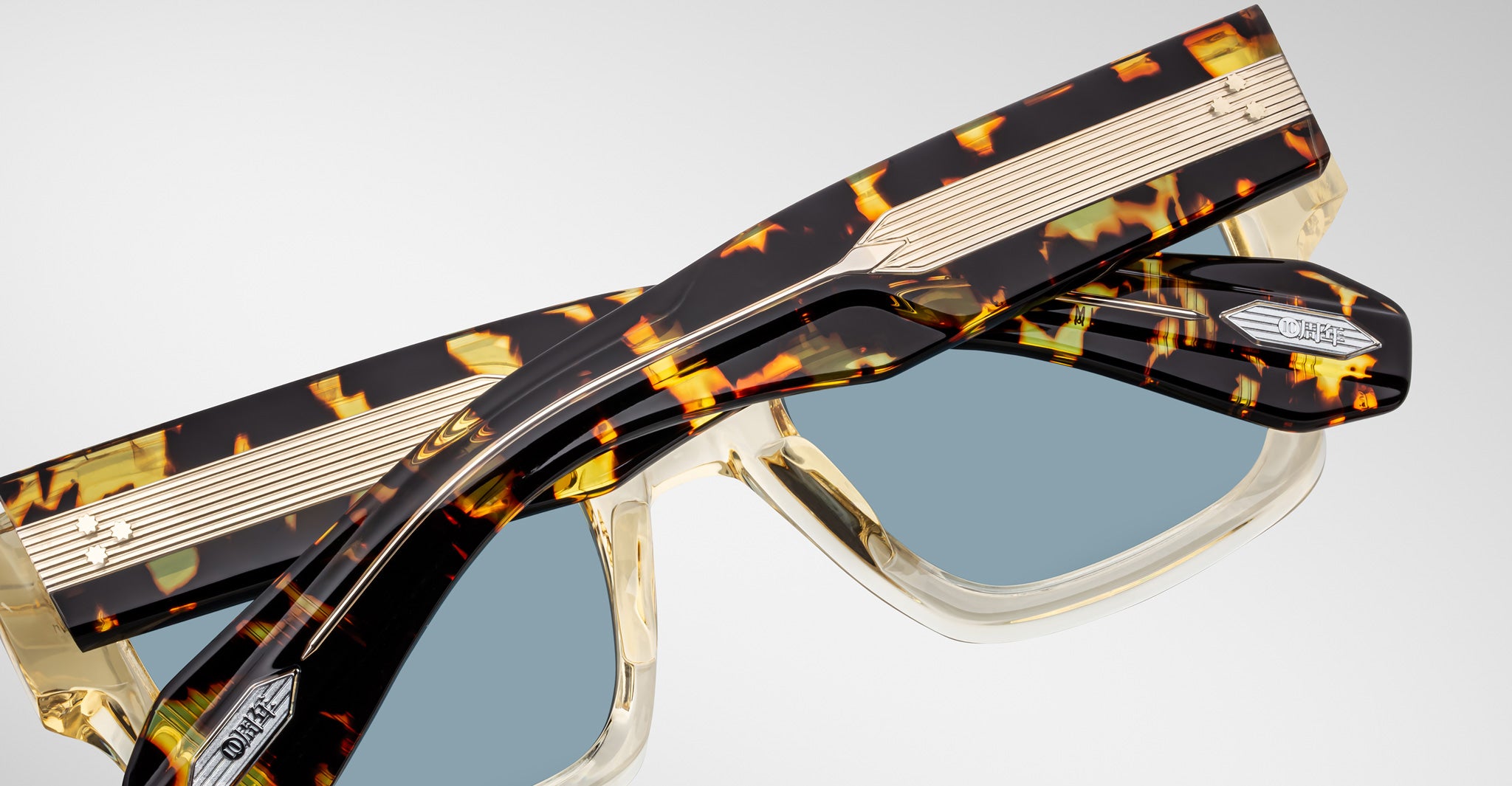 Close-up of Jacques Marie Mage Enzo sunglasses featuring tortoiseshell frames, metallic accents, and polarized blue-tinted lenses.