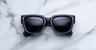 Jacques Marie Mage Enzo black rectangular sunglasses with dark lenses, viewed from above.