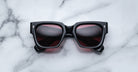 Jacques Marie Mage Enzo black square sunglasses with dark red lenses, viewed from above.