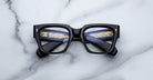 Jacques Marie Mage Enzo black rectangular eyeglasses with gold temples, top-down view.