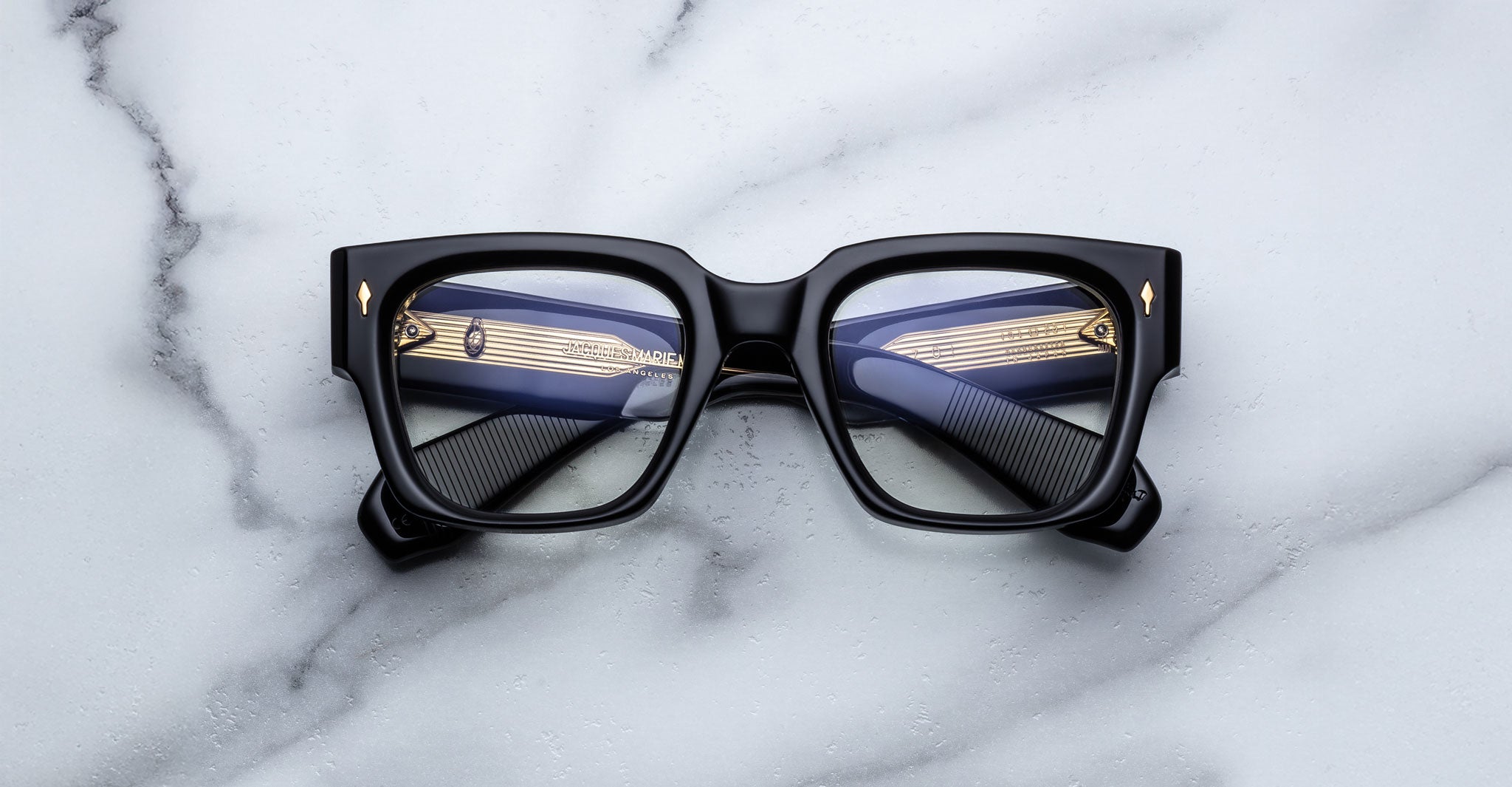 Jacques Marie Mage Enzo black rectangular eyeglasses with gold temples, top-down view.
