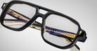 Close-up of Jacques Marie Mage Evans handcrafted optical glasses with an oversized acetate frame and gold and dark blue temple accents, set against a plain light background.