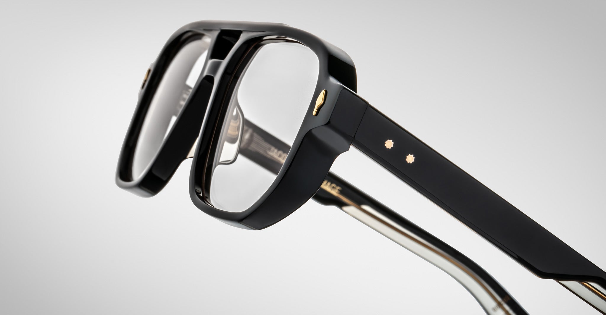 Close-up of the Jacques Marie Mage Evans glasses, showcasing black oversized acetate frames with gold accents and clear lenses against a plain light background.