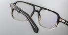 Close-up of Jacques Marie Mage Evans handcrafted black optical glasses with rectangular frames and clear lenses, highlighting temple and hinge details against a plain background.