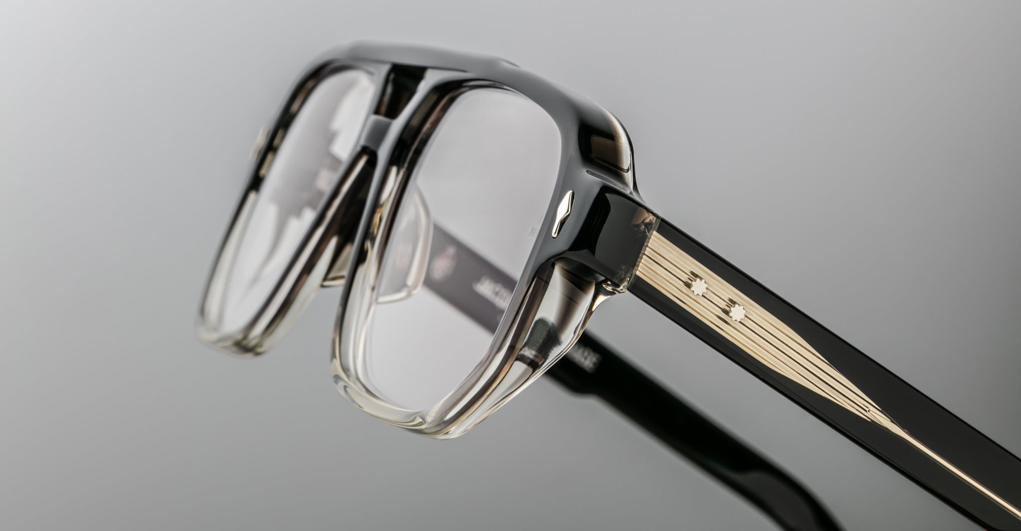 Close-up of the Jacques Marie Mage Evans optical glasses, handcrafted with an oversized black and clear acetate frame, gold accents, and decorative studs on the temples by Jacques Marie Mage, set against a neutral background.