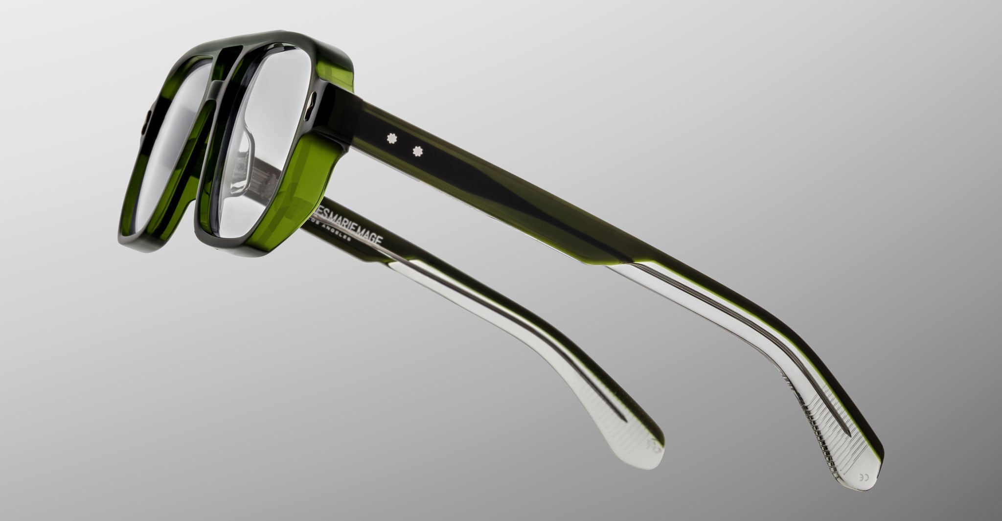 The Jacques Marie Mage Evans optical glasses feature handcrafted green and clear acetate rectangular frames, displayed against a gray gradient background.