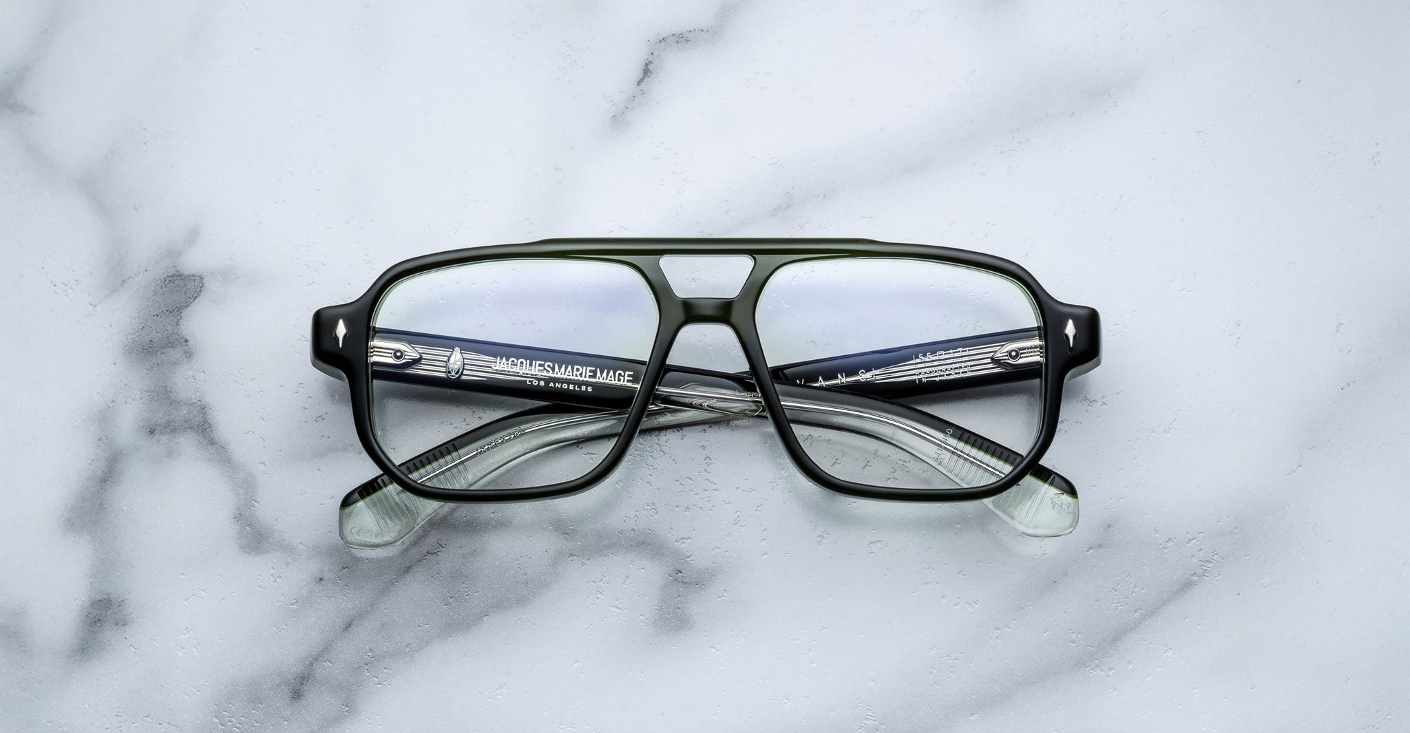 The Jacques Marie Mage Evans are black, rectangular handcrafted optical glasses with clear lenses and an oversized acetate frame by Jacques Marie Mage, displayed on a white marble surface.