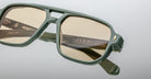 Close-up of green-framed Jacques Marie Mage Evans eyeglasses with tinted lenses, showcasing the brand name and model details engraved on the inner arms of these handcrafted optical glasses.