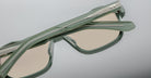 Close-up of Jacques Marie Mage Evans sunglasses: modern, light green acetate frames with beige lenses and overlapping hinges, shown against a neutral background and reflecting the distinctive Jacques Marie Mage style.