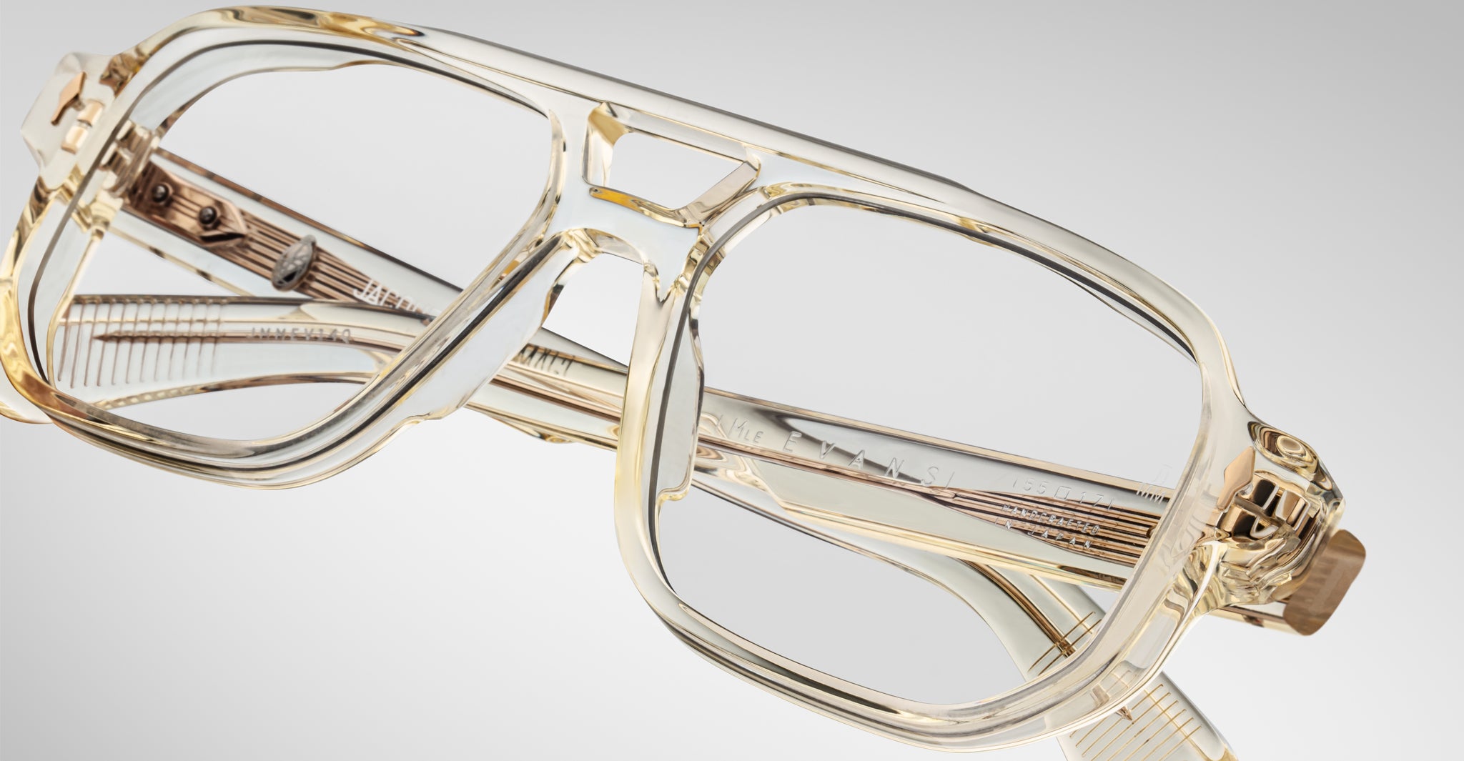 The Jacques Marie Mage Evans eyeglasses feature a clear, oversized acetate frame with thick, transparent rims and large lenses, showcased against a plain, light gray background.
