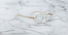 The Jacques Marie Mage Evans features clear, oversized acetate frames with rectangular lenses, elegantly displayed on a white marble surface.