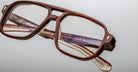 Close-up of Jacques Marie Mage Evans glasses, featuring a brown oversized rectangular acetate frame with brand markings on the temples, set against a plain light background.