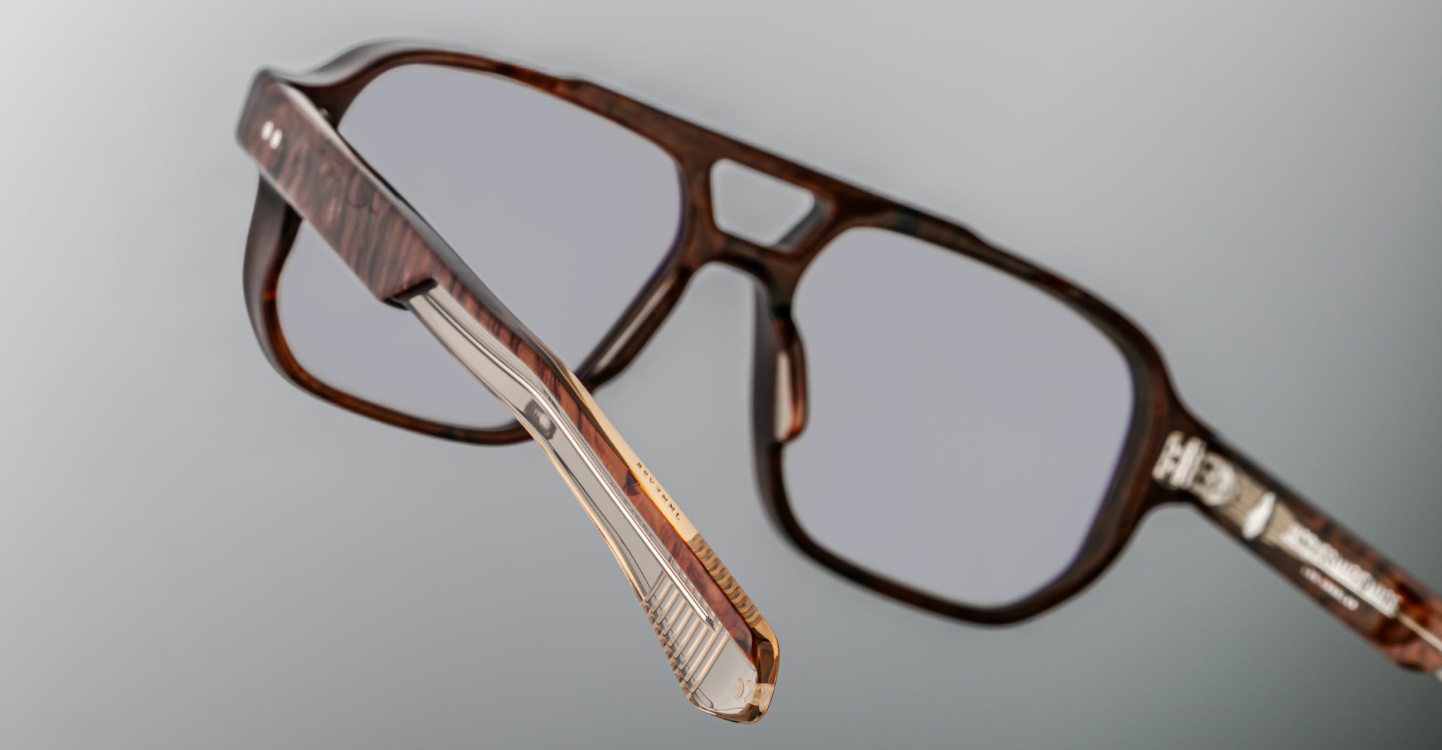 Close-up of Jacques Marie Mage Evans brown eyeglasses featuring clear lenses, an oversized acetate frame, and a detailed temple hinge, set against a gray background.