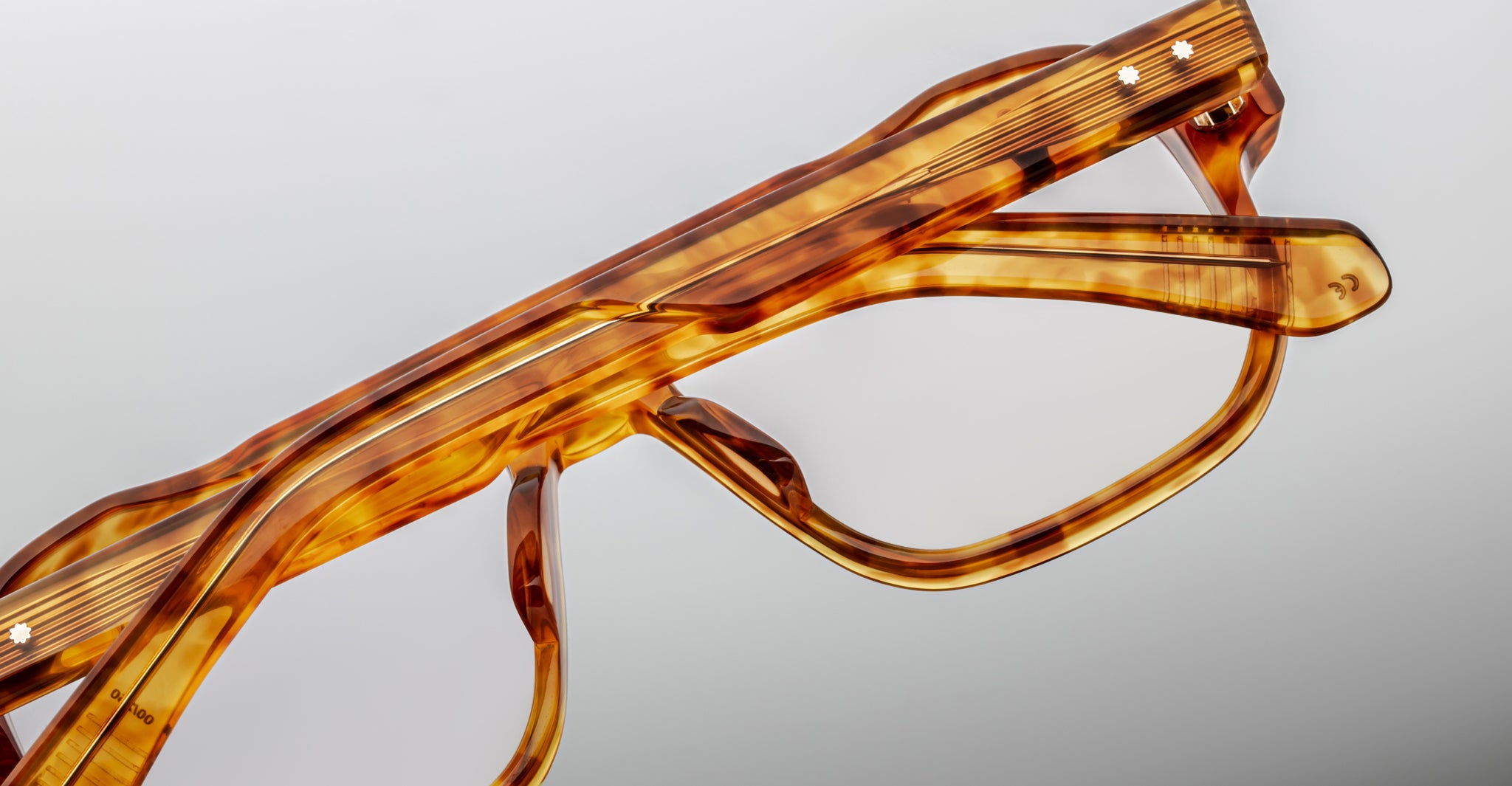Close-up of the top half of Jacques Marie Mage Evans handcrafted optical glasses, showcasing an oversized brown acetate frame against a plain, light background.