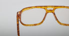 Close-up of Jacques Marie Mage Evans optical glasses, featuring amber tortoiseshell acetate with clear lenses in an oversized handcrafted frame, shown against a plain light background.