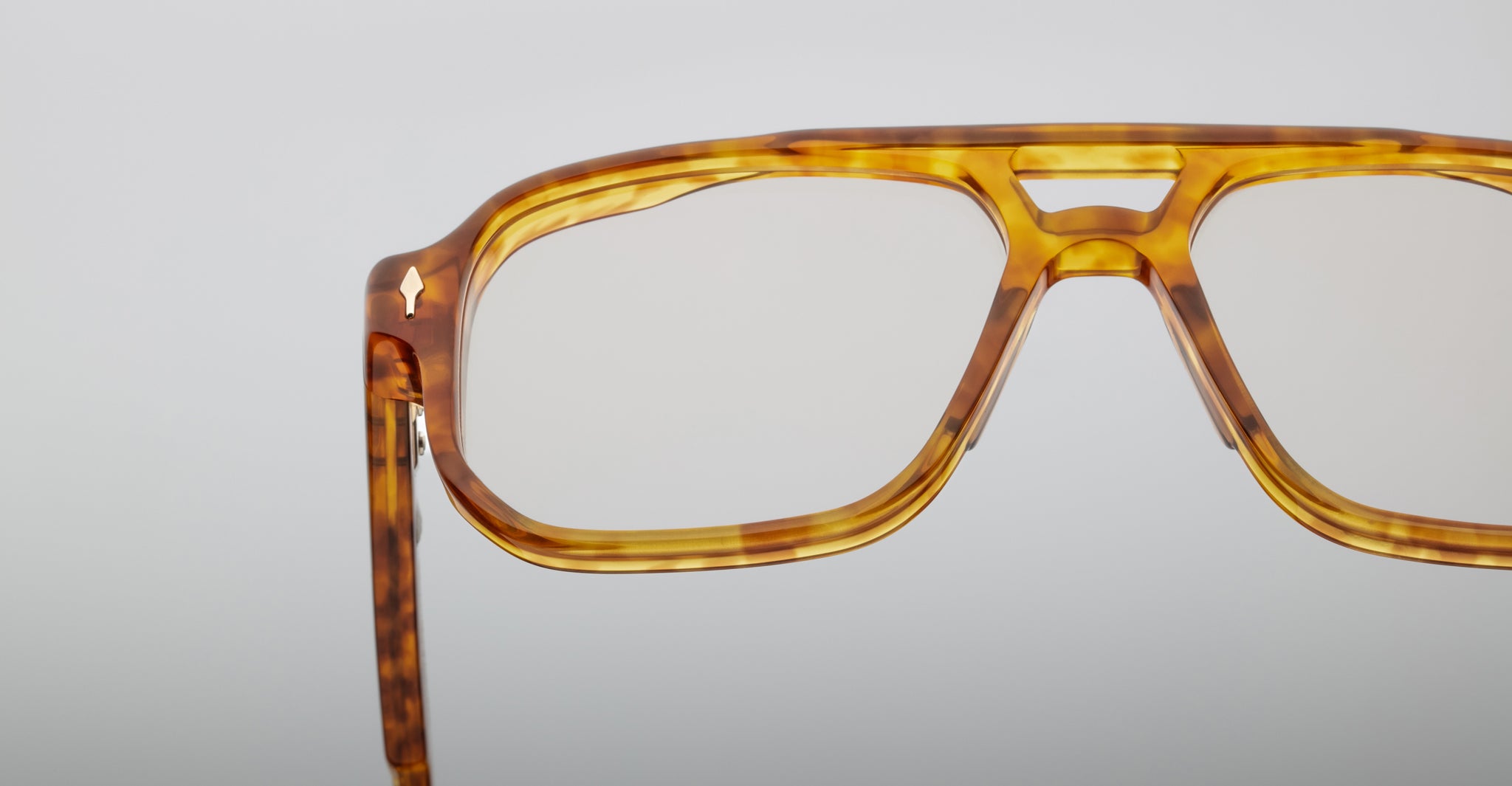 Close-up of Jacques Marie Mage Evans optical glasses, featuring amber tortoiseshell acetate with clear lenses in an oversized handcrafted frame, shown against a plain light background.