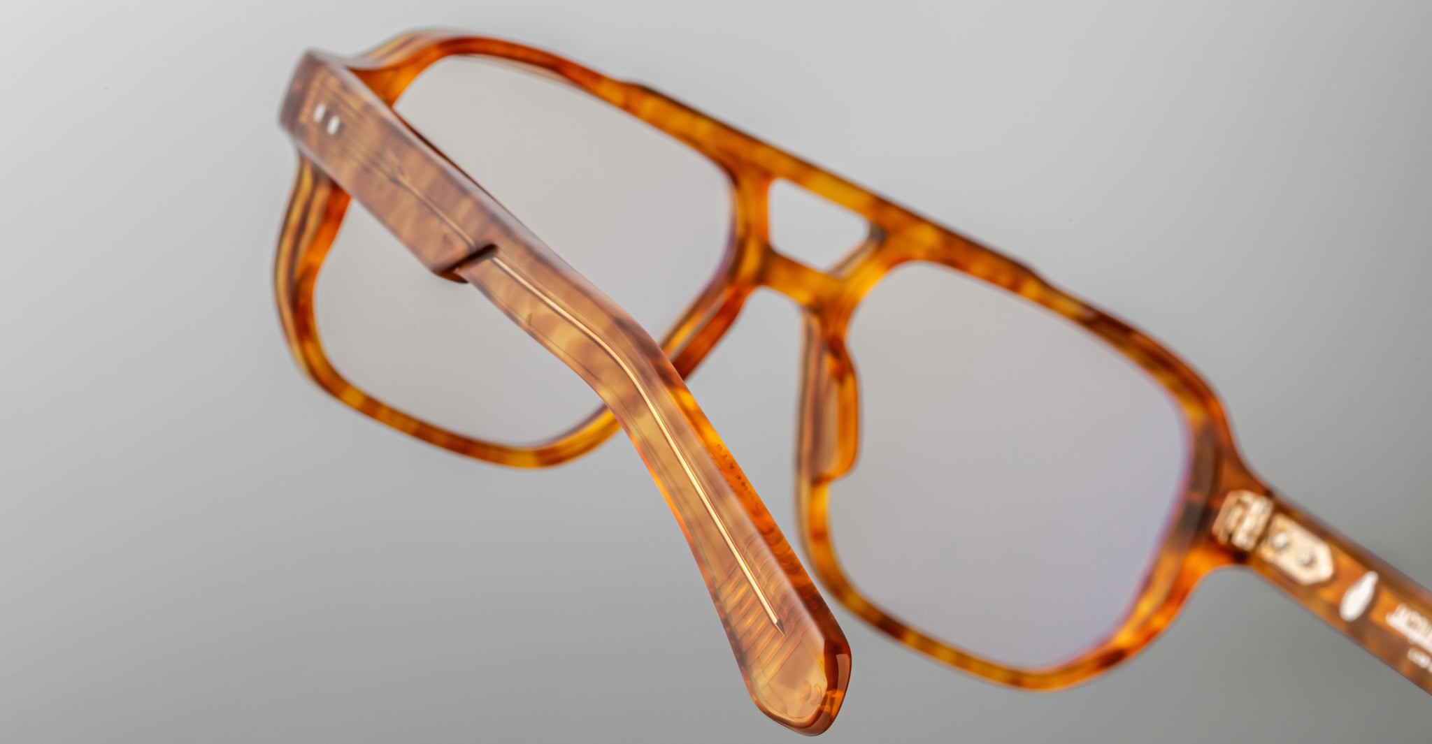Close-up of Jacques Marie Mage Evans handcrafted optical glasses, featuring an oversized brown tortoiseshell acetate frame with clear lenses, showcasing detailed frame and temple design against a plain background.