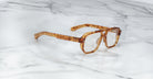 Jacques Marie Mage Evans oversized acetate eyeglasses in brown tortoiseshell by Jacques Marie Mage are displayed on a white marble surface, highlighting their handcrafted optical style.