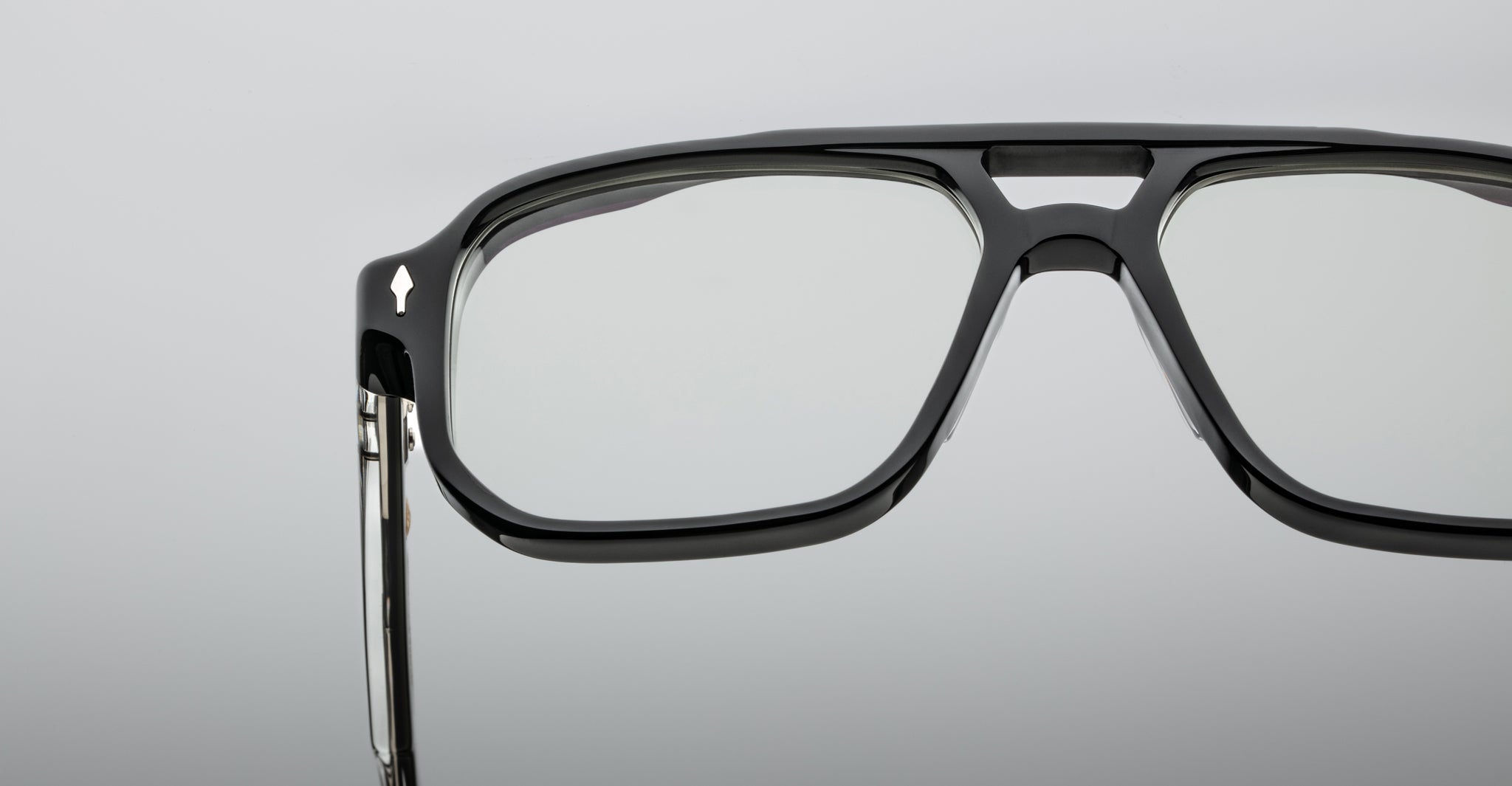 Close-up of the upper half of Jacques Marie Mage Evans, black thick-rimmed oversized acetate eyeglasses with clear lenses, set against a plain gray background.