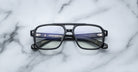 The Jacques Marie Mage Evans handcrafted black rectangular optical glasses with clear lenses rest on a white marble surface, highlighting the brand’s details in the oversized acetate frame.