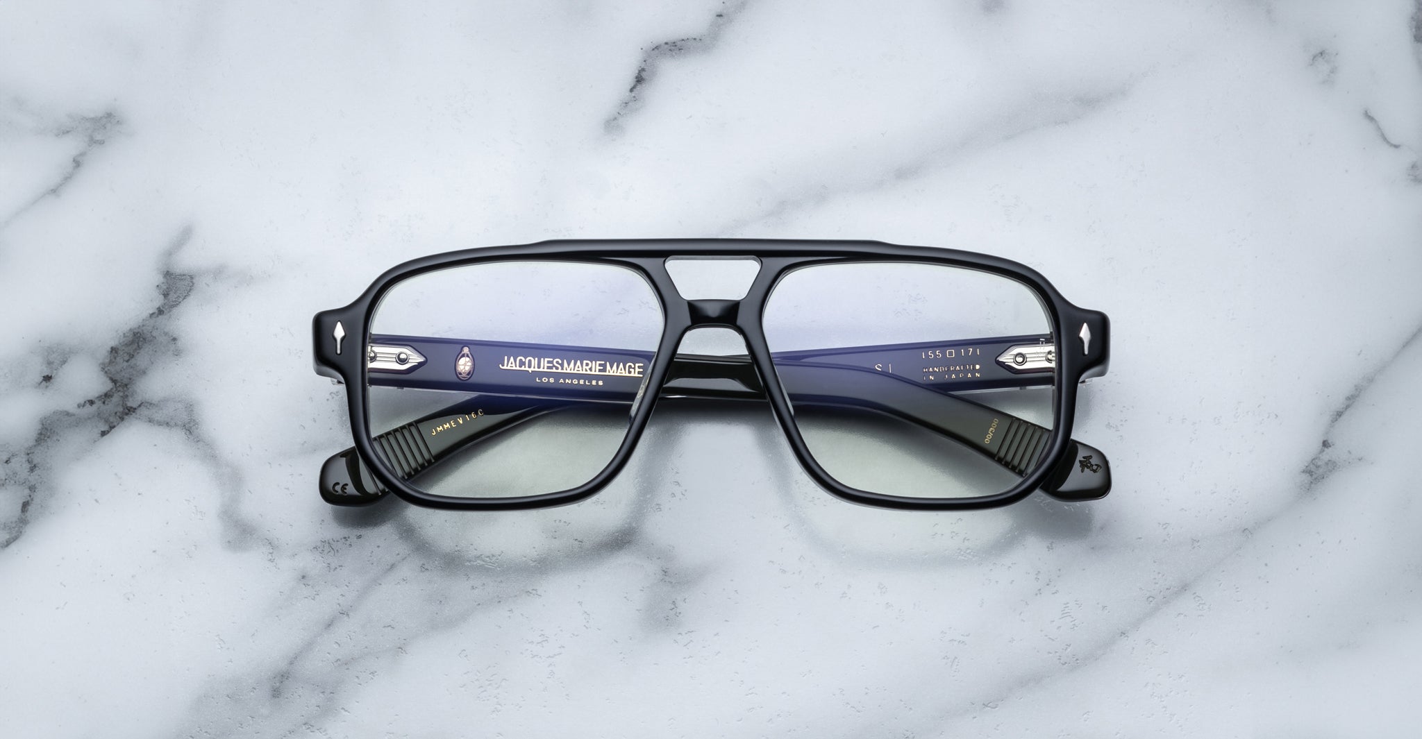 The Jacques Marie Mage Evans handcrafted black rectangular optical glasses with clear lenses rest on a white marble surface, highlighting the brand’s details in the oversized acetate frame.