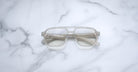 The Jacques Marie Mage Evans eyeglasses by Jacques Marie Mage feature oversized, translucent square acetate frames and are displayed on a white marble surface.
