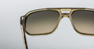 Close-up of Jacques Marie Mage Evans sunglasses featuring an oversized acetate frame in translucent khaki with brown gradient lenses, set against a plain light background.