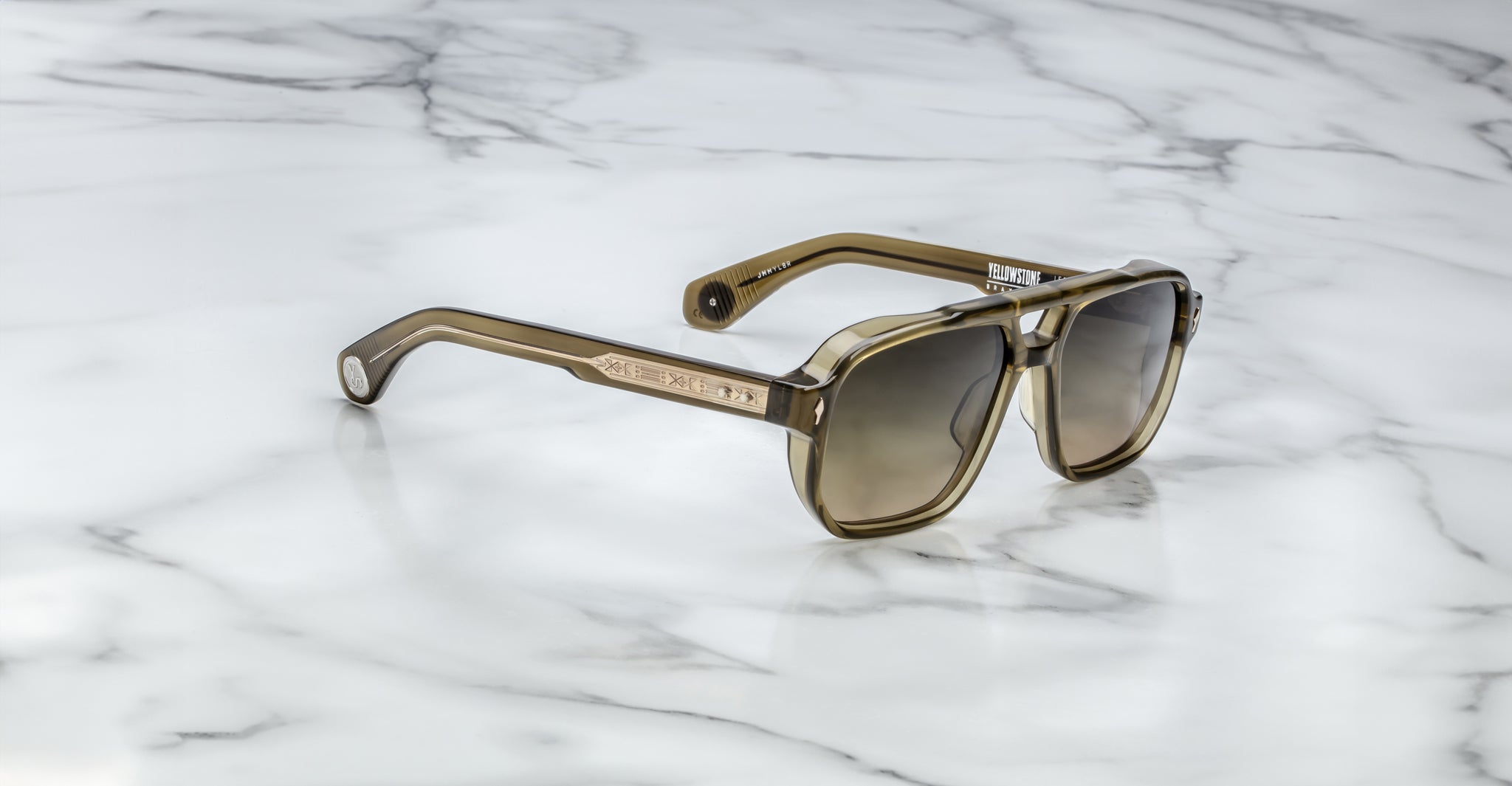 The Jacques Marie Mage Evans sunglasses, featuring oversized rectangular acetate frames in a brown tint, rest on a white marble surface.