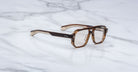 A pair of Jacques Marie Mage Evans brown tortoiseshell rectangular eyeglasses with clear lenses and an oversized acetate frame rests on a white marble surface.