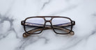 The Jacques Marie Mage Evans eyeglasses by Jacques Marie Mage feature a brown, oversized rectangular acetate frame, displayed on a white marble surface.