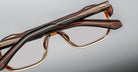 Close-up of two handcrafted Jacques Marie Mage Evans optical glasses with oversized brown acetate frames, stacked against a neutral background.