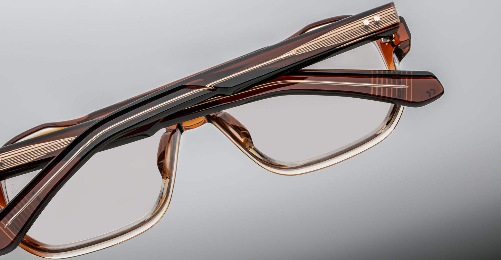 Close-up of two handcrafted Jacques Marie Mage Evans optical glasses with oversized brown acetate frames, stacked against a neutral background.