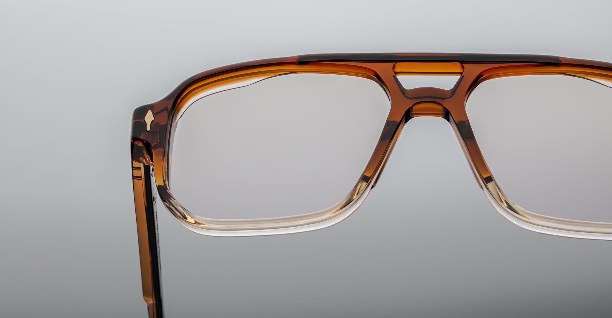 Close-up of the upper half of Jacques Marie Mage Evans optical glasses by Jacques Marie Mage, featuring rectangular frames in brown and clear acetate, set against a plain gray background.