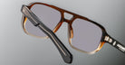 Close-up of Jacques Marie Mage Evans handcrafted brown optical glasses with gray tinted lenses, showcasing detailed black arm accents against a neutral background.