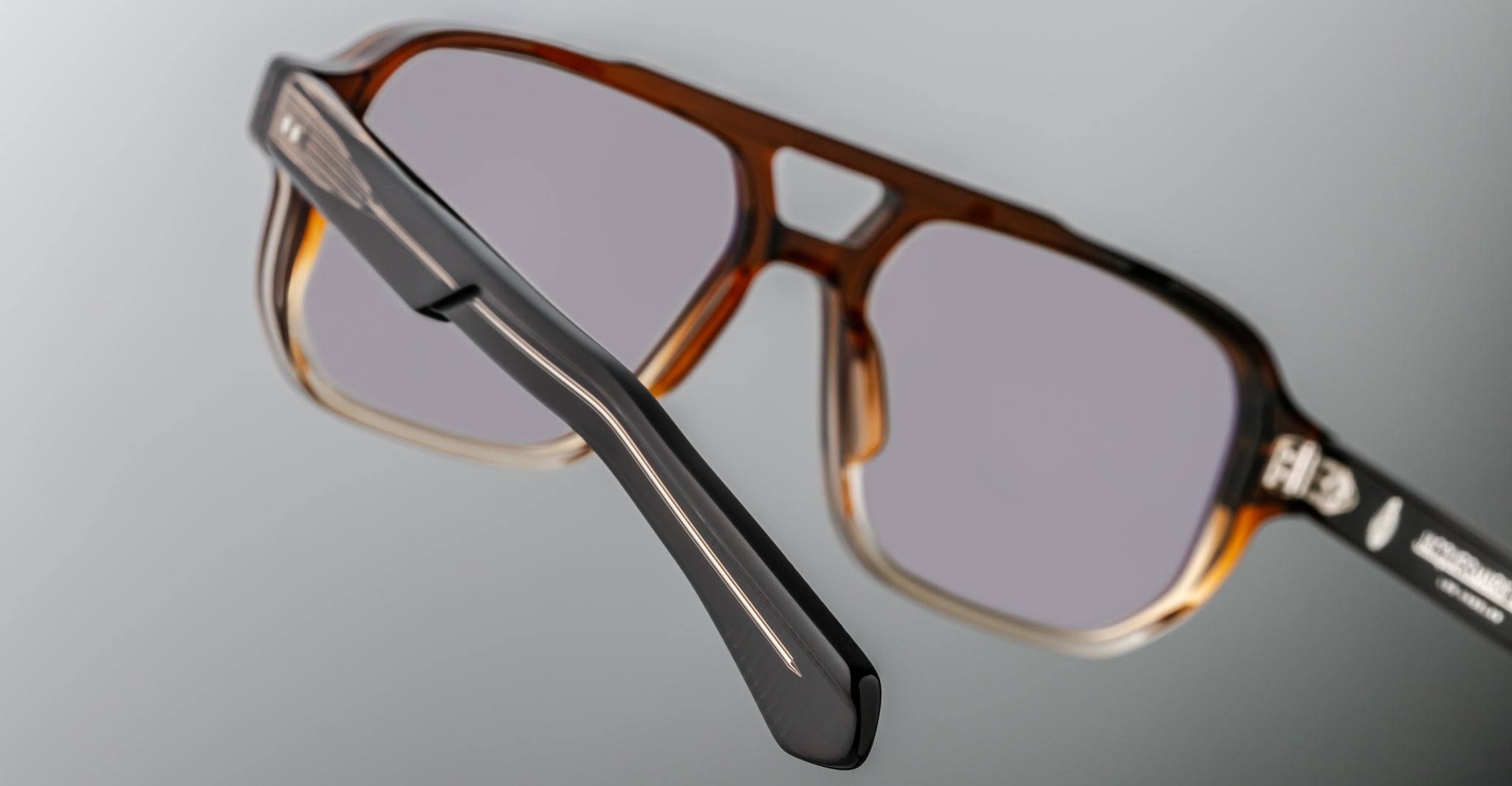 Close-up of Jacques Marie Mage Evans handcrafted brown optical glasses with gray tinted lenses, showcasing detailed black arm accents against a neutral background.