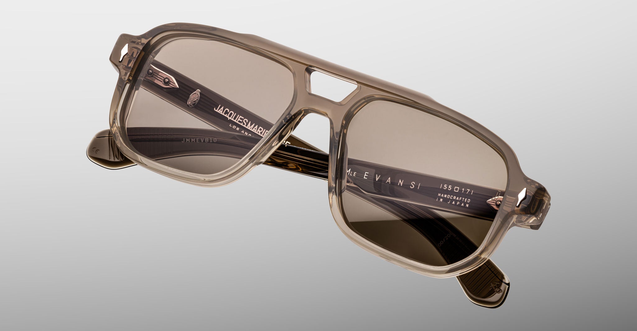 The Jacques Marie Mage Evans sunglasses feature a rectangular, taupe acetate oversized frame with dark tinted lenses, inspired by Jacques Marie Mage design, shown on a light gray background.