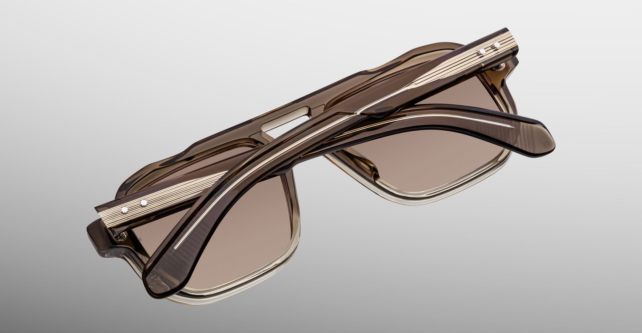 Jacques Marie Mage Evans sunglasses feature folded brown oversized acetate frames with gold temple accents, echoing the brand's signature handcrafted style, presented against a plain gradient background.